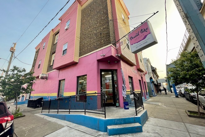 A corner building in the Kensington neighborhood of Philadelphia is painted bubblegum pink with bright blue concrete steps to enter. Above the door hangs a sign that says "Pound Cake Heaven."