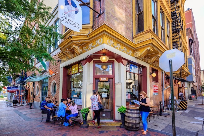 Outside Franklin Fountain, an old-fashioned corner ice cream shop in Old City Philadelphia, people mill about, some seated and eating ice cream.