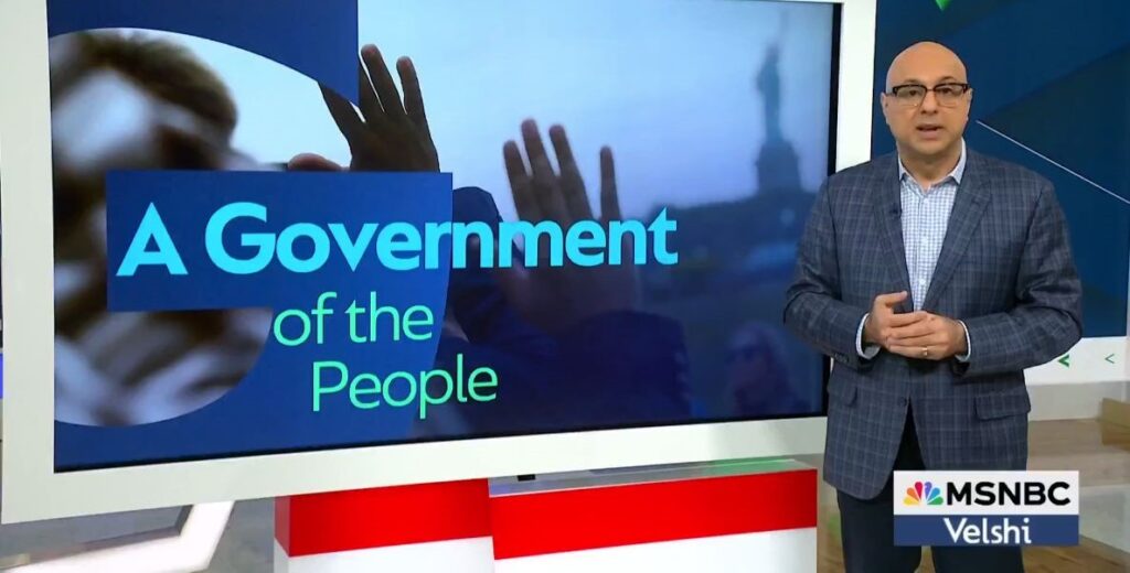 Ali Velshi, a bald man in glasses and a gray suit, stands to the right of a monitor that reads A Government of the People as he discusses Citizenship Day