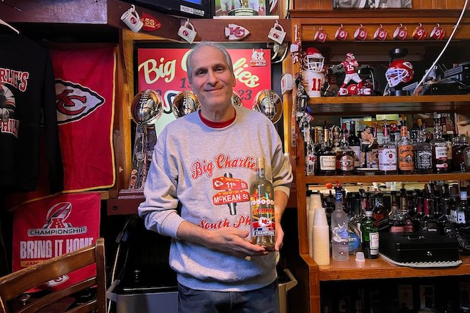 Inside Big Charlie's Saloon, a Kansas City Chiefs theme bar in South Philly, a white man wearing a Chiefs sweatshirts stands in front of a wall full of Chiefs memorabilia.