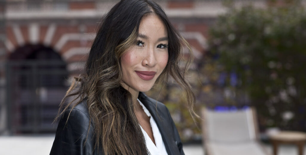 Binh Nguyen, a Vietnamese woman with long, curled hair, wearing lipstick, a black leather jacket and white blouse, by Reuben Harley.