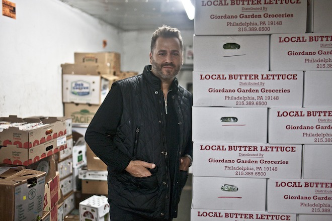 Marcello Giordano, a white man wearing all black, stands with hands in his pockets next to cardboard crates of butter lettuce.