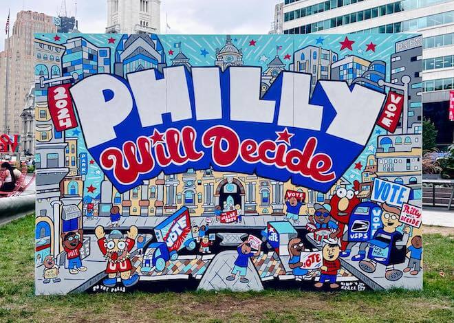 A red, white and blue mural says "2024 PHILLY Will Decide," with Phillies font, Philadelphia skyscrapers and landmarks, and people holding signs that say "VOTE."