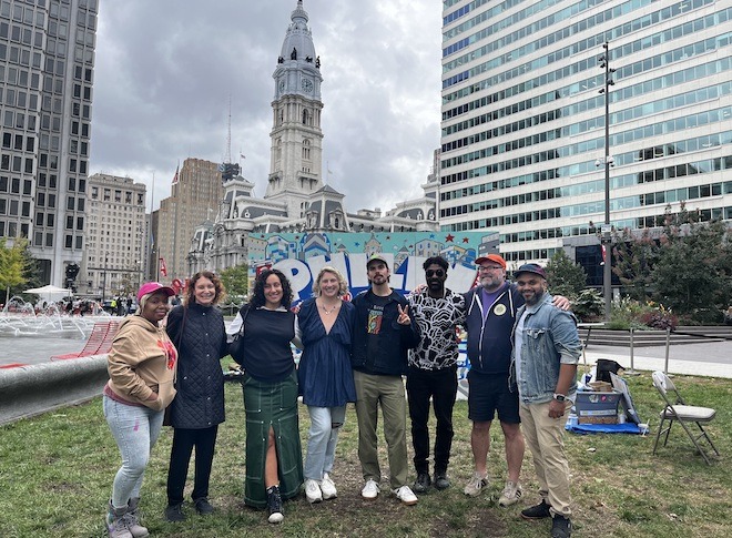 Artists Serena Saunders, Jane Golden, Isabella Akhtarshenas, Nicole Nikolich, Conrad Benner, Ailoyius McIlwaine, Hawk Krall, Jeffy Thomas stand in front of a Philly Votes painting and City Hall for To the Polls, a pro-voting art exhibition in LOVE Park in Philadelphia.