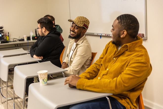 Four adults sit at desks in a classroom. They are students in a Skills Initiative cohort.