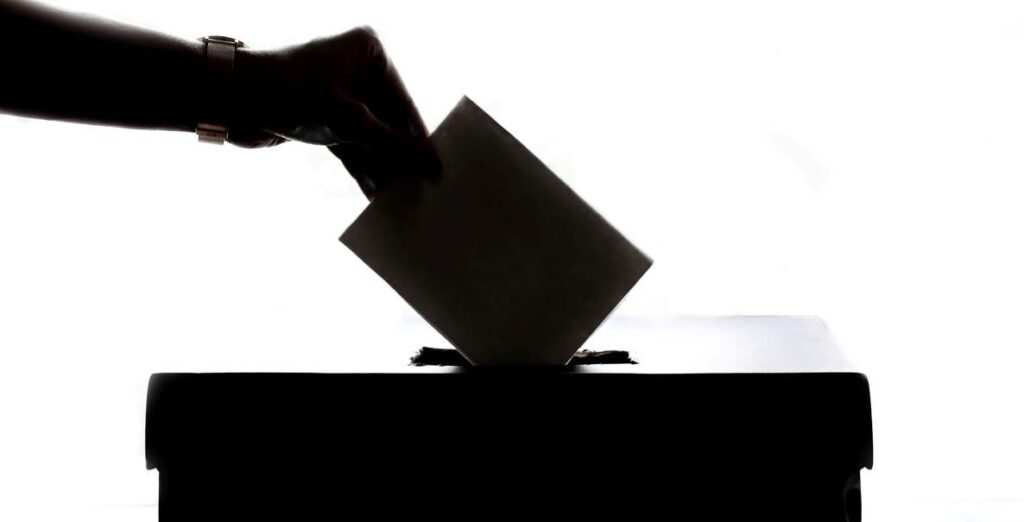 A silhouette of a hand holding a rectangular slip and inserting it into a ballot box