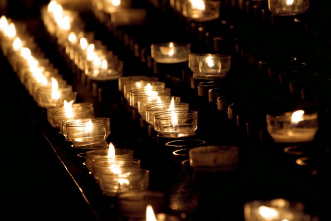 rows of small lit candles burn in the dark