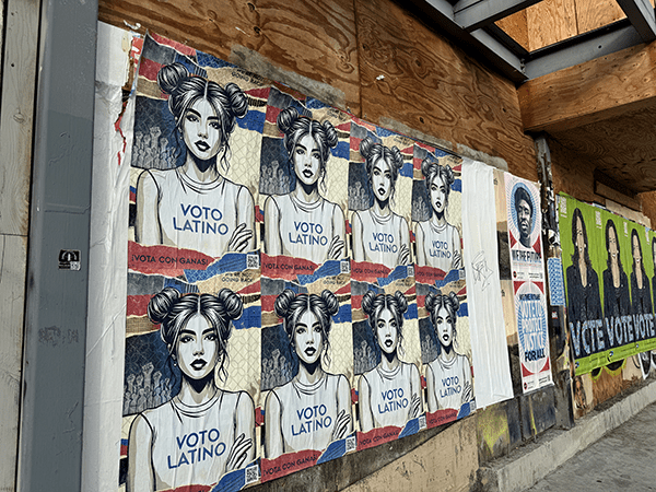 Multiple wheatpaste get-out-the-vote signs 11th and Spring Garden streets contain illustrations of a woman with two buns in her hair, wearing a sleeveless t-shirt that says "VOTO LATINO." By Olivia Kram.