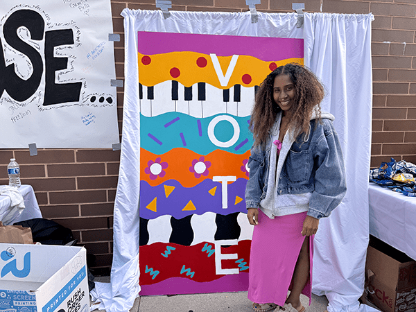 Arshayla Robinson of Art-Making at the Polls stands in front of her mural at West Philadelphia High School. By Olivia Kram