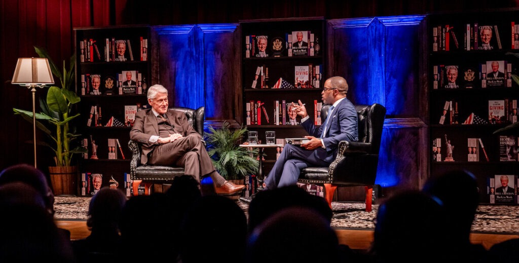 Former President Bill Clinton and Jonathan Capehart onstage, in a library setting.