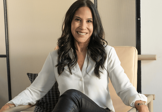 Dr. Jaime Zuckerman, a white woman with long brown wavy hair, wearing a white blouse, sits in a beige chair and smiles. 