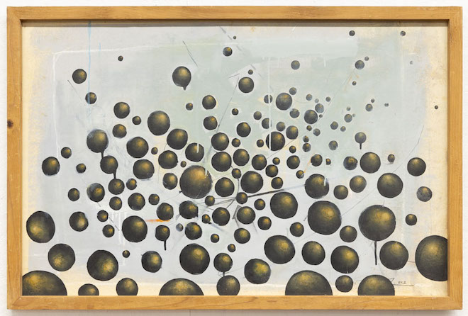 A framed, untitled work featuring dozens of dark gold orbs by Spel, an incarcerated artist.