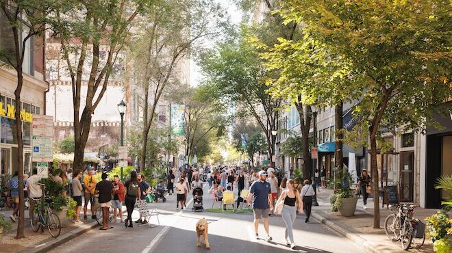 Pedestrians, some with dogs, walk along a tree-lined open Walnut Street in Philadelphia on a day when the street closed to vehicular traffic.