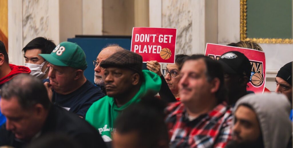 People sit inside Philadelphia City Council chambers in City Hall during a committee of the whole meeting on legislation to allow the Sixers to build an arena in Center City. Some hold signs saying "DON'T GET PLAYED."