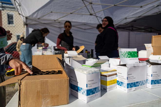 A table of wound care supplies in boxes stands outside an open tent where people are standing around. Free wound care is offered at The Love Lot, organized by Volunteering Untapped Philadelphia and The Everywhere Project on Nov. 9, 2024.