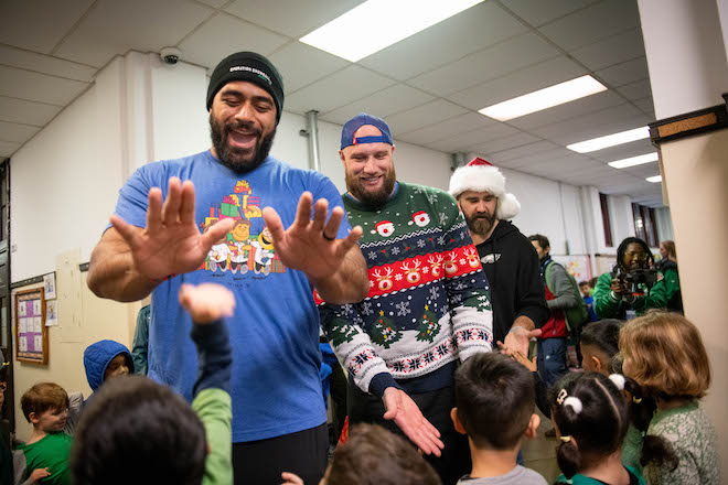 Eagles players Jordan Mailata, Lane Johnson and Jason Kelce dressed in Christmas gear, give high fives to school children as part of Operation Snowball.