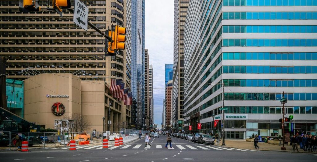 A street view in Philadelphia showing two people in the middle of a crosswalk and tall office buildings rising like canyons on either side of the street