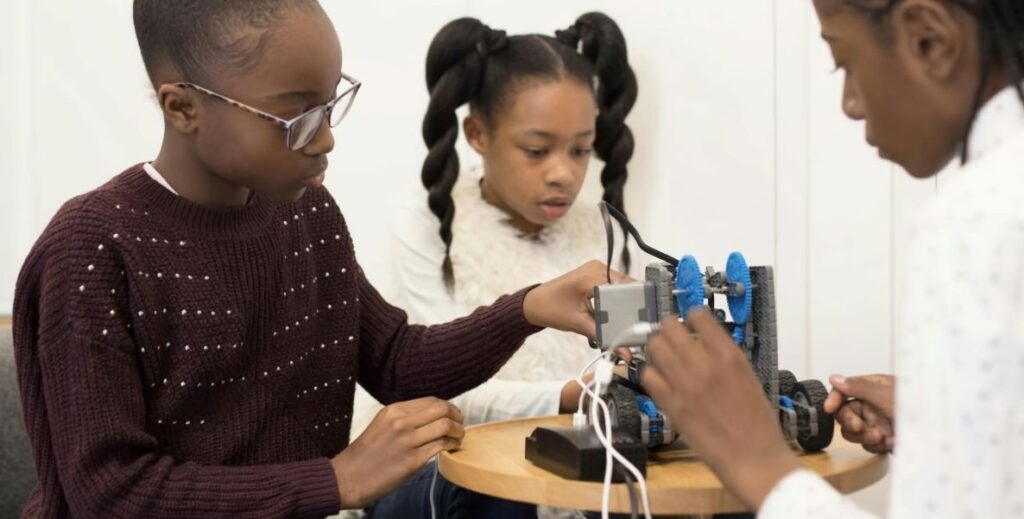 Three Black children sit around a table building a robot model