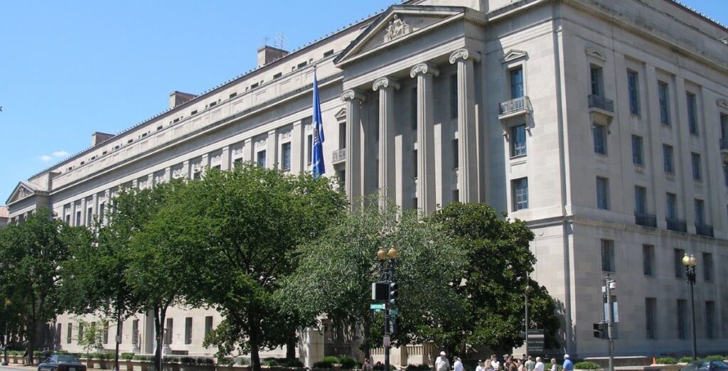 A multi-story light gray stone edifice with columns in front on the right side. It's the Robert F. Kennedy Department of Justice Building, headquarters of the U.S. Department of Justice.