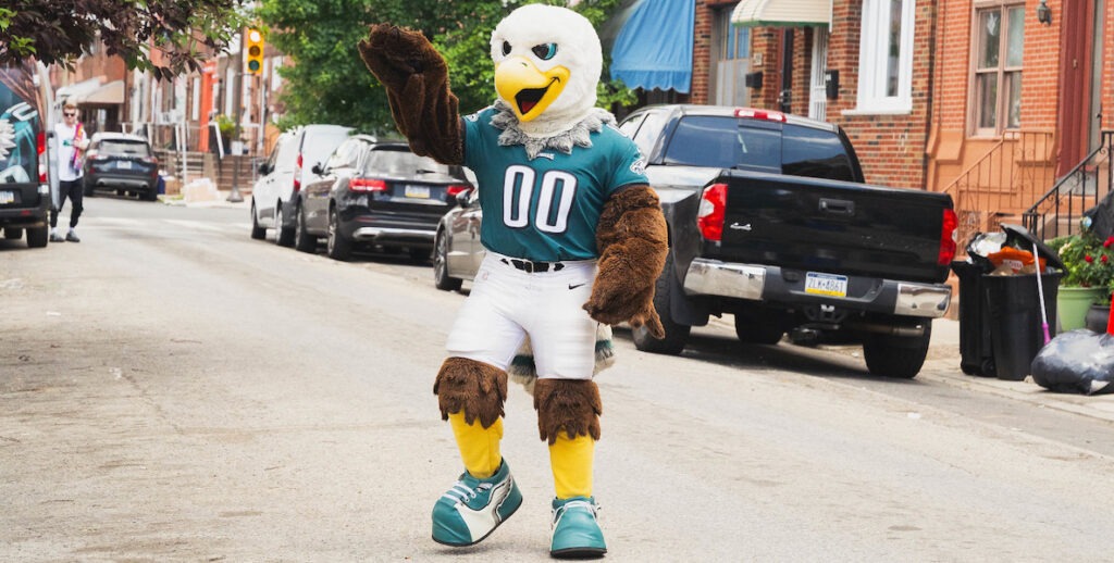 Eagles mascot Swoop, an Eagle wearing an 00 Eagles jersey and green and white sneakers, walks in the street in South Philadelphia.