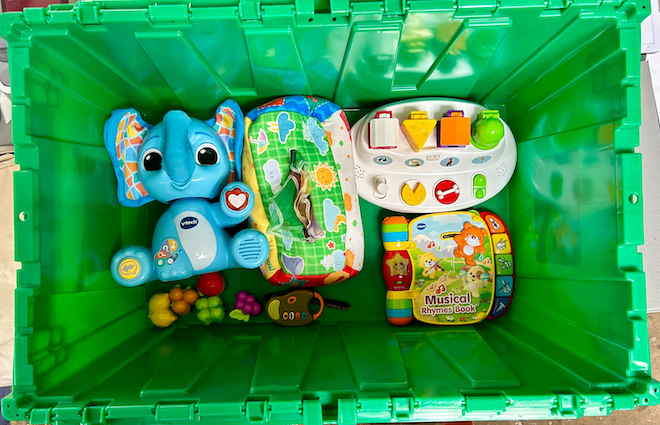 A green plastic bin is open to reveal plastic baby toys.