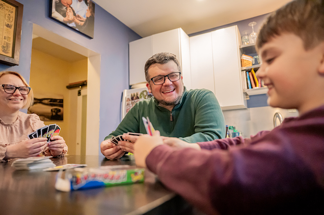 Game night at the Gijunis home with, left to right: Rebecca, Joe and Gabe, playing Uno at a kitchen table.
