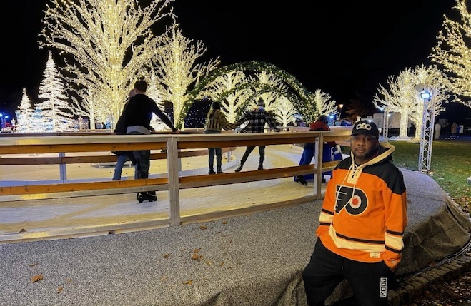 Jovace Nelson, a Black man in a Flyers jersey and black pants, stands outside an ice-less skating rink at FDR Park in December 2023.