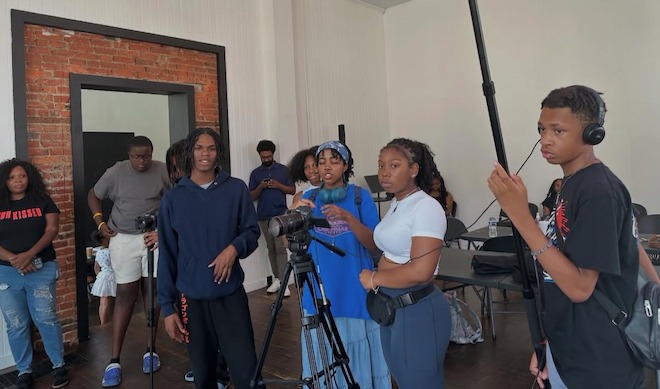 High school students stand in a room, behind cameras and holding a boom microphone for 5 Shorts Project's 'Bout Mine I Matter summer program shoot a documentary.