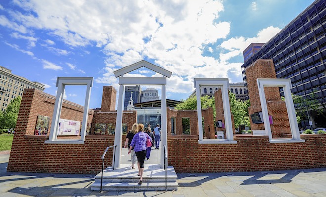 Under a bright blue sky with clouds, The open-air President’s House in Independence National Historical Park.