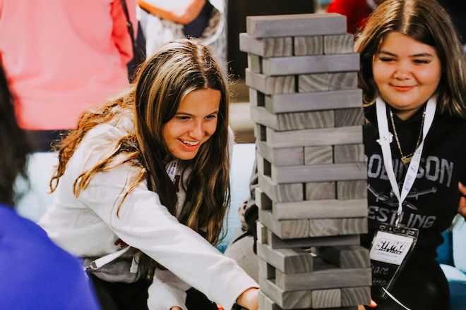 Two high school age white girls play Jenga. 
