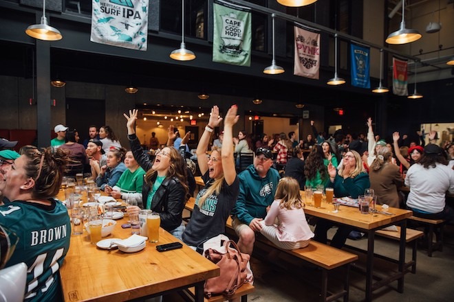 Yards Brewing Co., a large beer hall with banners, holds large picnic tables of families wearing Eagles gear on a game day.
